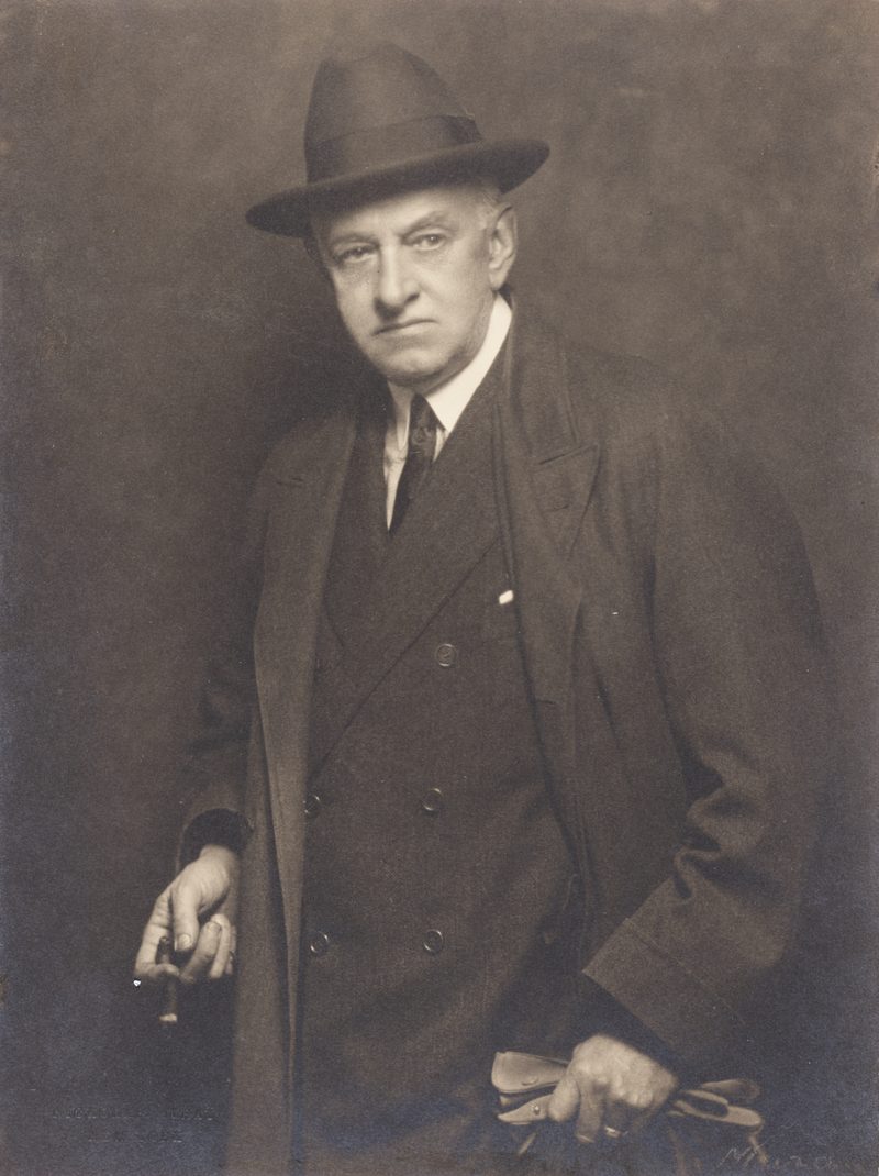 Photograph of a gray-haired man in a dark suit and hat