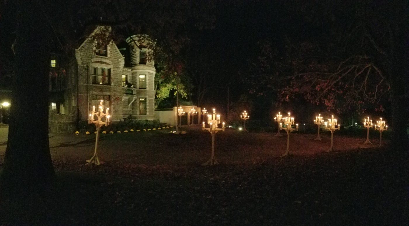 A row of lit candelabras across the lawn with the house behind