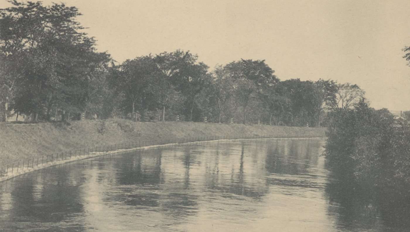A broad canal with grassy, tree-lined banks and still water