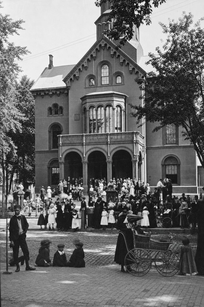A large crowd gathered in front of an arched brick courthouse