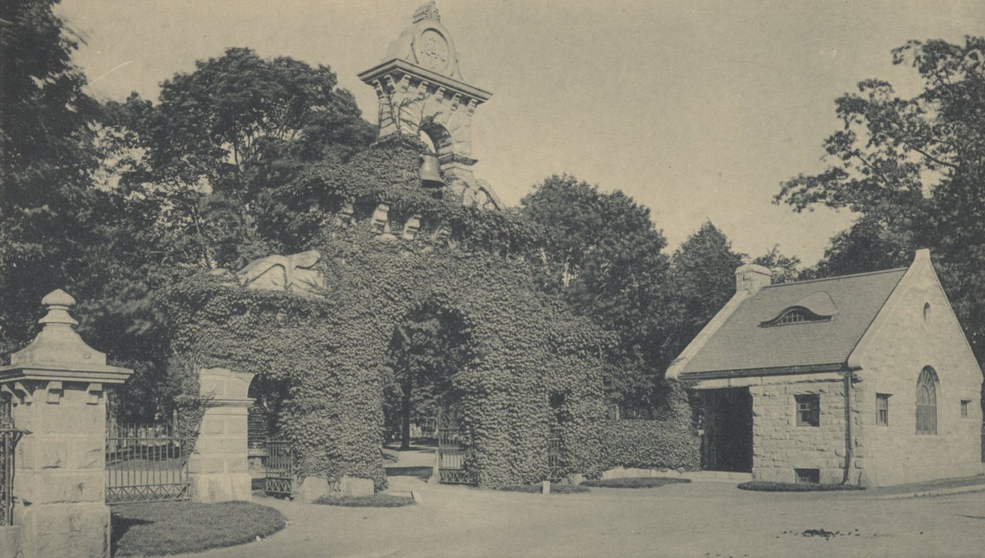 An ivy-covered stone gateway with a small stone lodge beside it, under tall trees