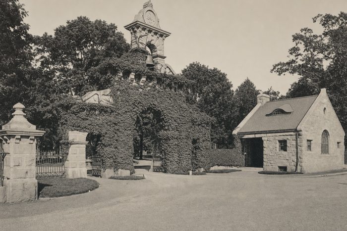 An ivy-covered stone gateway with a small stone lodge beside it, under tall trees