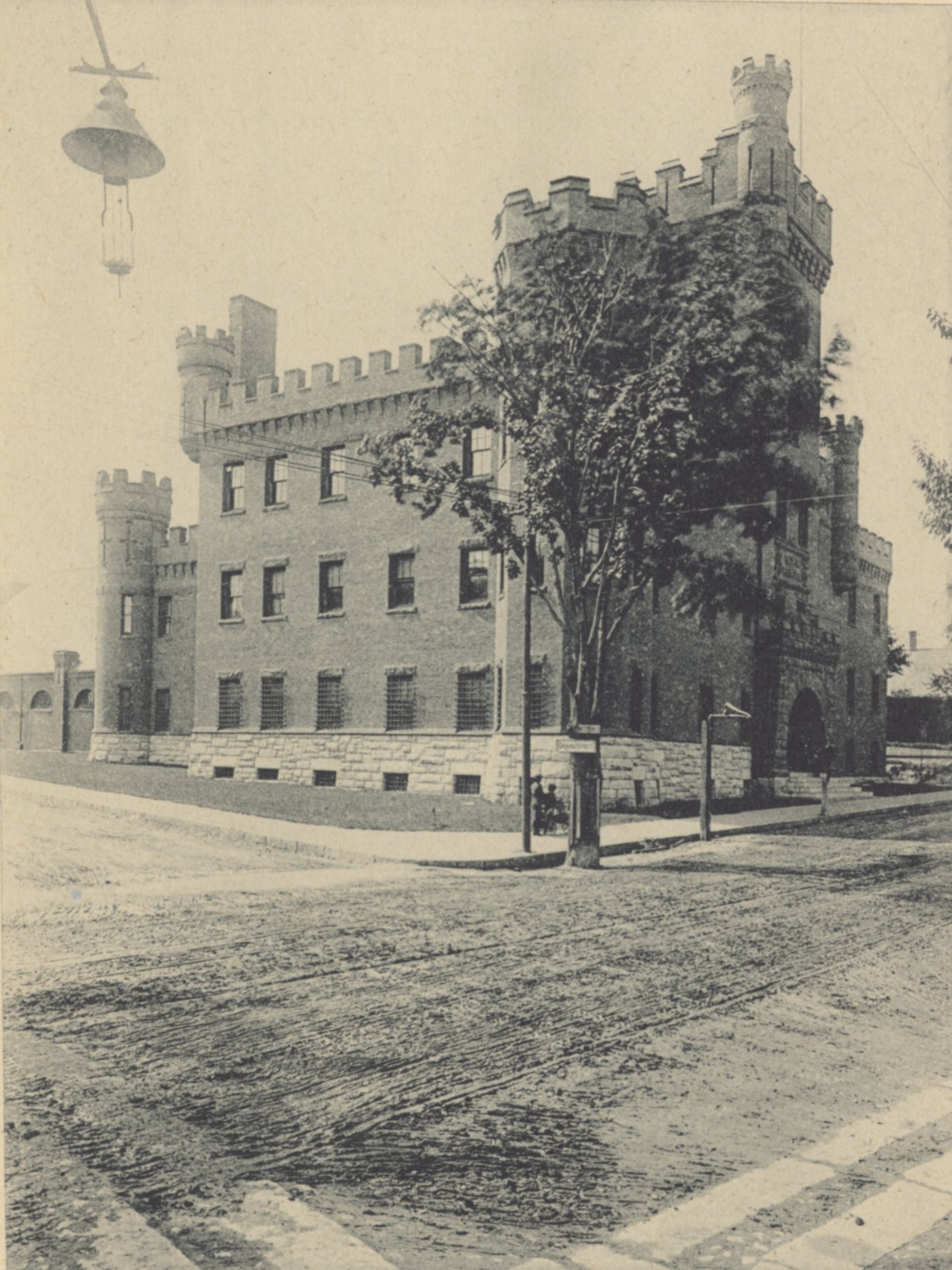 A brick armory with castle-like battlements and towers at a street corner, with a street lamp