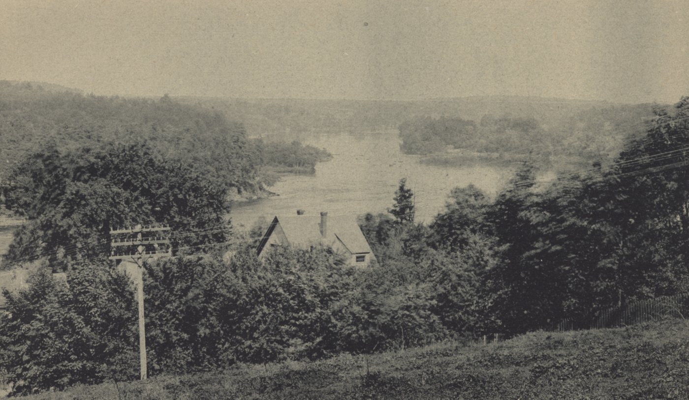 View from a wooded height down to a wide bend of the Merrimack River, with a signpost in the foreground