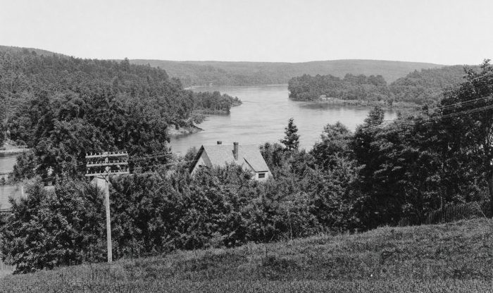 View from a wooded height down to a wide bend of the Merrimack River, with a signpost in the foreground