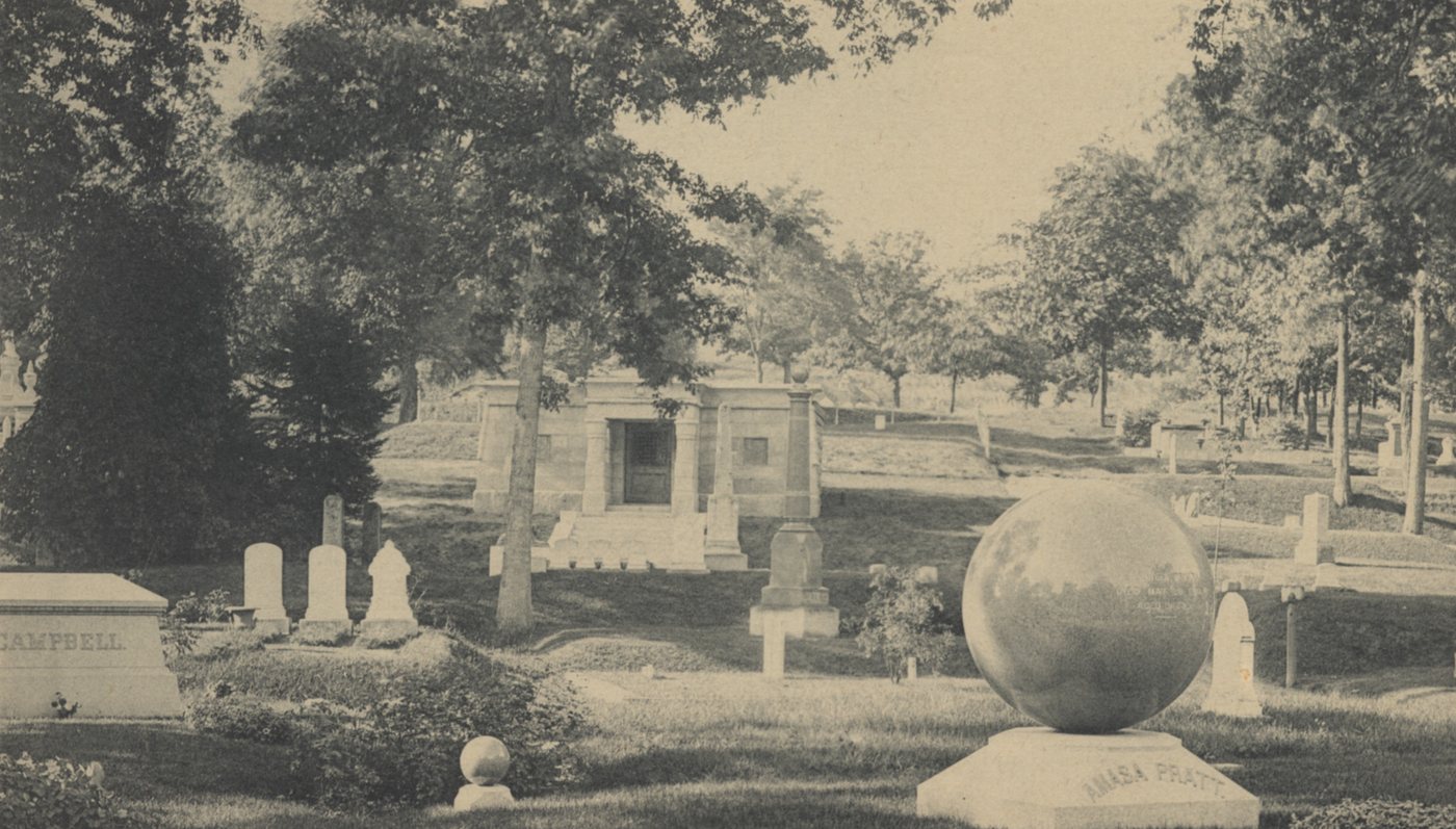 Cemetery lawn with monuments, headstones and a large stone sphere on a pedestal