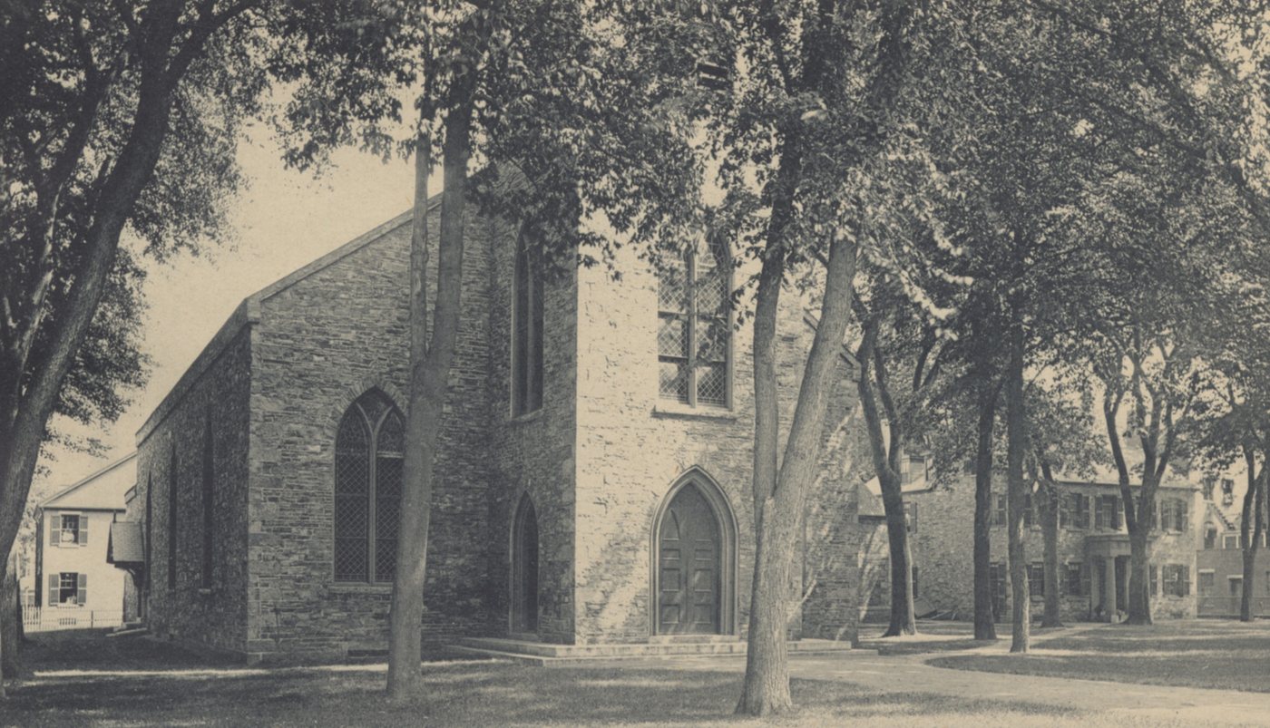 A gray stone church with pointed windows under tall trees