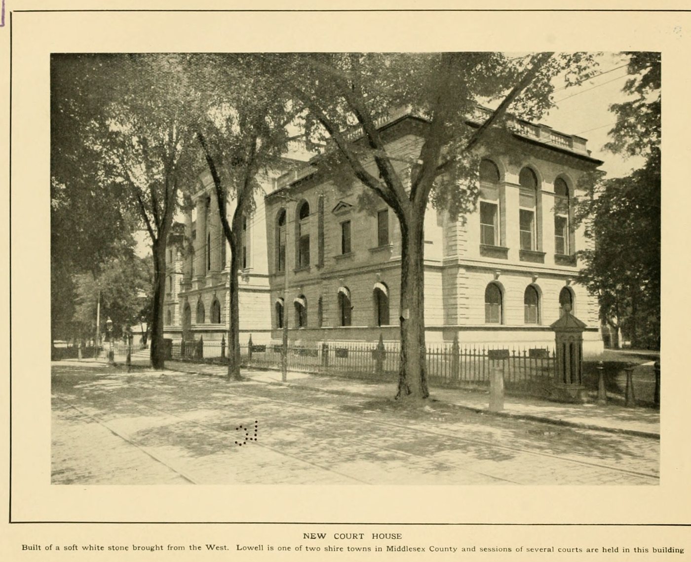 A classical stone courthouse behind tall trees and an iron fence