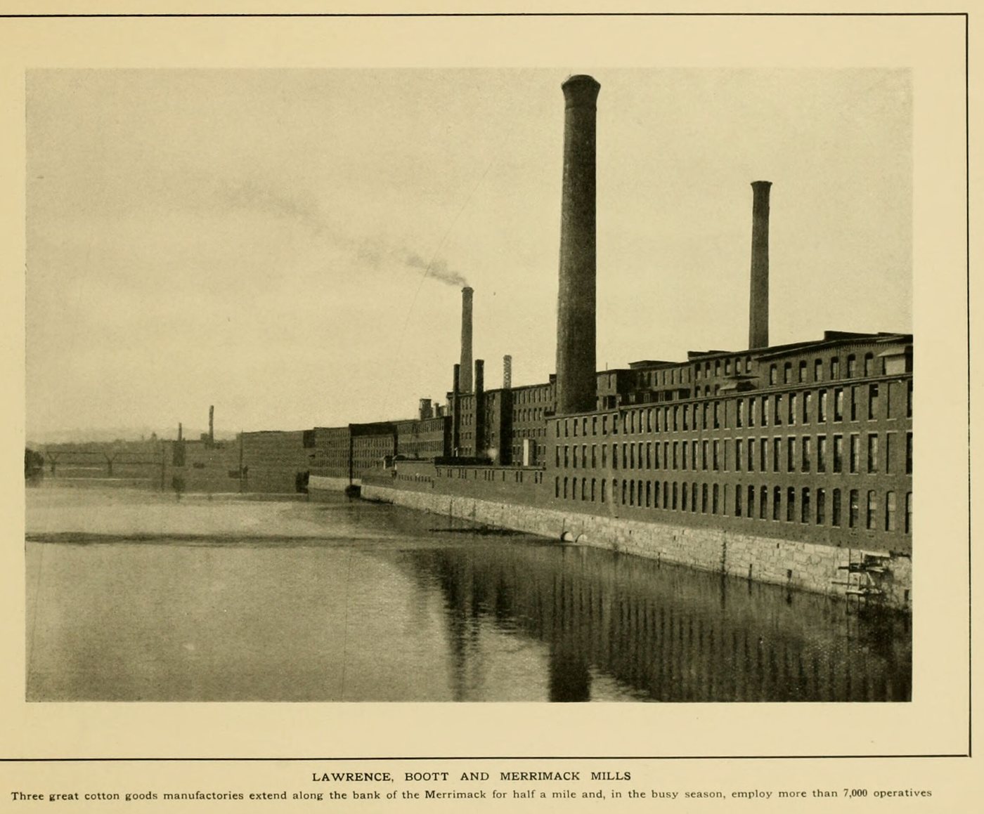 Tall smokestacks and a long brick mill along the water, smoke drifting from a chimney