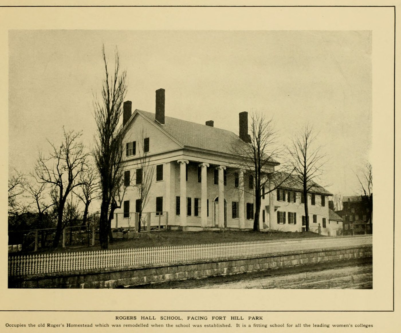 A white columned house with two chimneys behind a fence and bare trees
