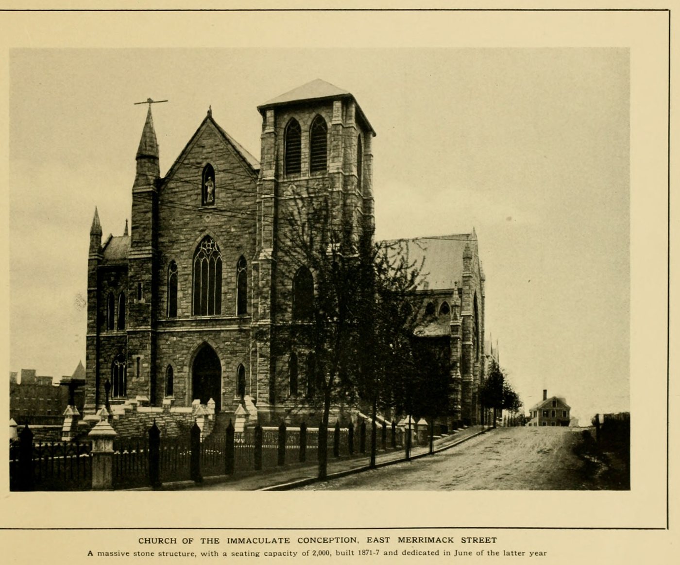 A large stone church with a square tower and a spire behind an iron fence
