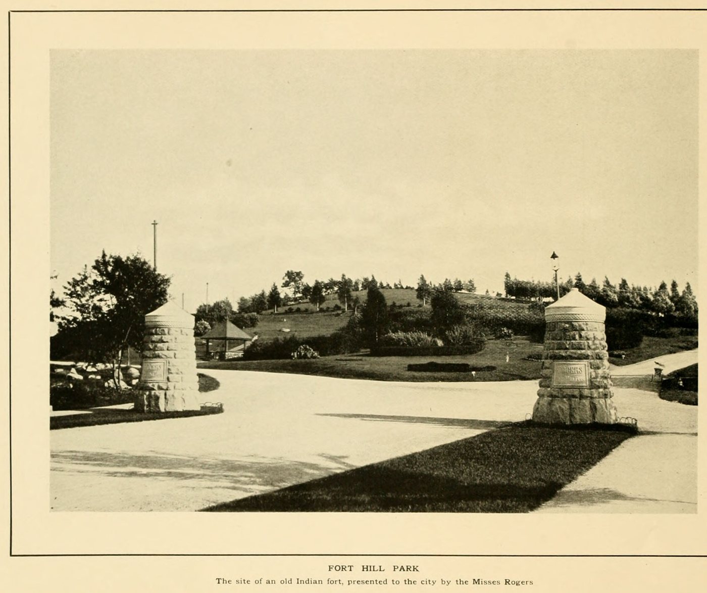 Park entrance with two round stone gate towers, curving paths and a planted hill