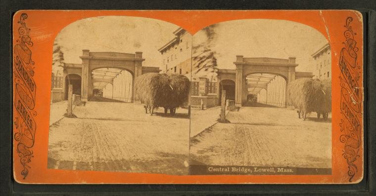 Stereograph of an arched gateway at the end of a bridge, with a horse-drawn wagon loaded with hay