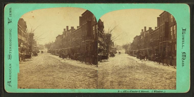 Stereograph of a snowy street lined with brick buildings, with sleighs and wagons