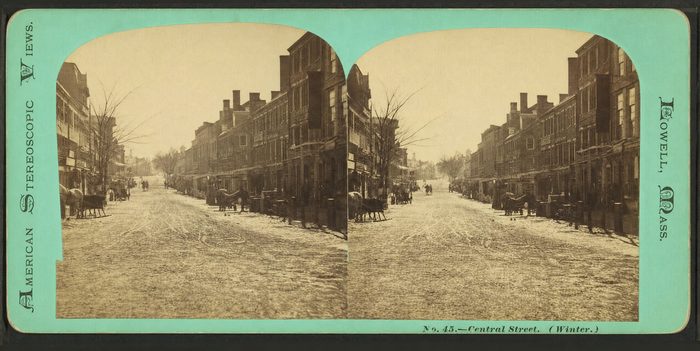 Stereograph of a snowy street lined with brick buildings, with sleighs and wagons