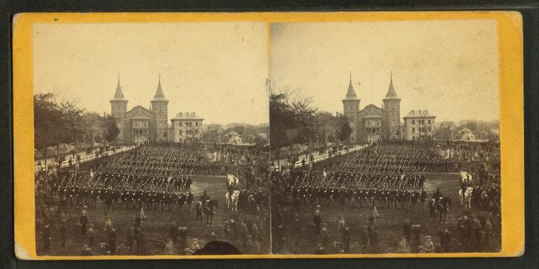 Stereograph of ranks of soldiers drilling on a common, with a towered building in the distance