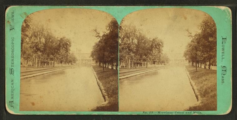 Stereograph of a straight canal lined with trees, with mill buildings in the distance