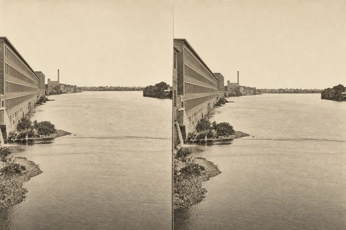 Stereograph of the river with long mill buildings along the left bank