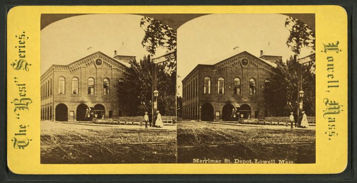 Stereograph of a brick railroad depot with arched openings and a carriage in front