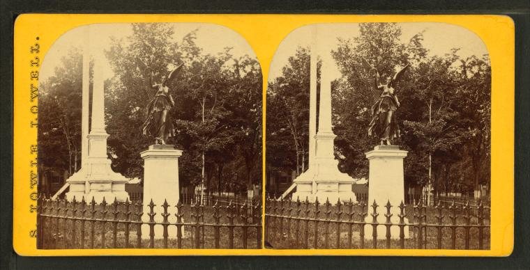 Stereograph of a tall obelisk and a statue on a pedestal behind an iron fence, with trees