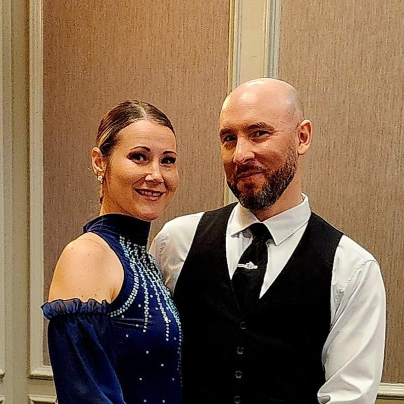 Perry in a white shirt, black vest and bow tie standing beside Sherri in a navy-and-white ballroom gown, both smiling