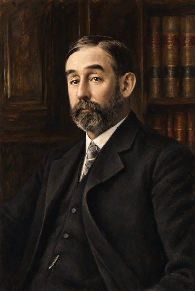 Oil portrait of a man with a trimmed beard, in a dark three-piece suit, before shelves of books