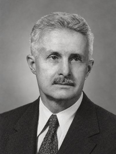 Black-and-white portrait of a man in his fifties with short gray hair and a mustache, in a dark suit, white shirt and patterned tie