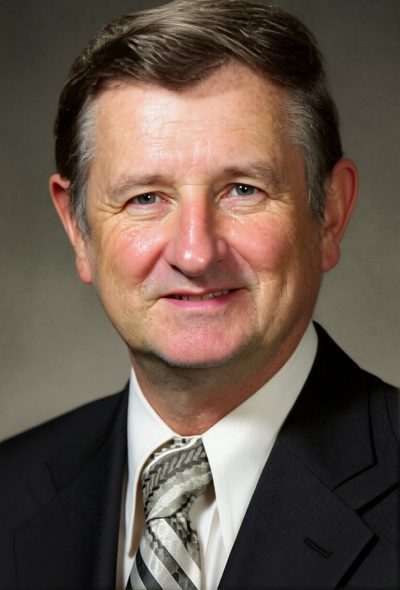Color portrait of a smiling gray-haired man in a dark suit, white shirt and patterned tie